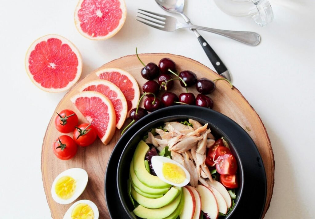 healthy food A vibrant breakfast flat lay featuring a mix of fruits, avocado, eggs, tomatoes, and sliced meats on a wooden platter.